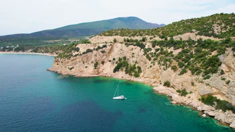 Vista-Aérea-De-Un-Velero-Anclado-Rodeado-De-Agua-Clara,-Altos-Acantilados-Y-Vegetación-Mediterránea,-Isla-De-Thassos,-Grecia,-Europa