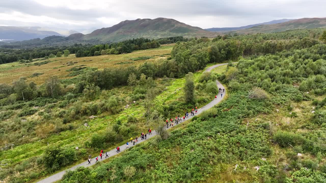 스코틀랜드의 원추형 언덕을 향해 길을 따라 걷는 등산객들의 공중 전망