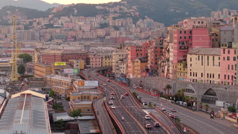 aerial view of genoa, italy, busy highway with cars, colorful buildings, port area and hills in background during sunset