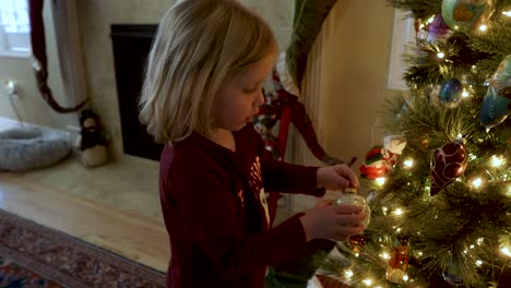 adorable niña de tres años decorando el árbol de navidad junto a la chimenea