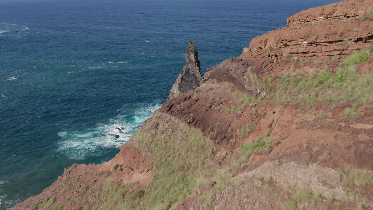 Flying over mountainside to reveal volcanic rock in vast blue ocean during sunny day cinematic epic feeling