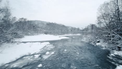 Aerial-shot-of-frozen-river-and-hanging-bridge-in-frosty-winter-morning