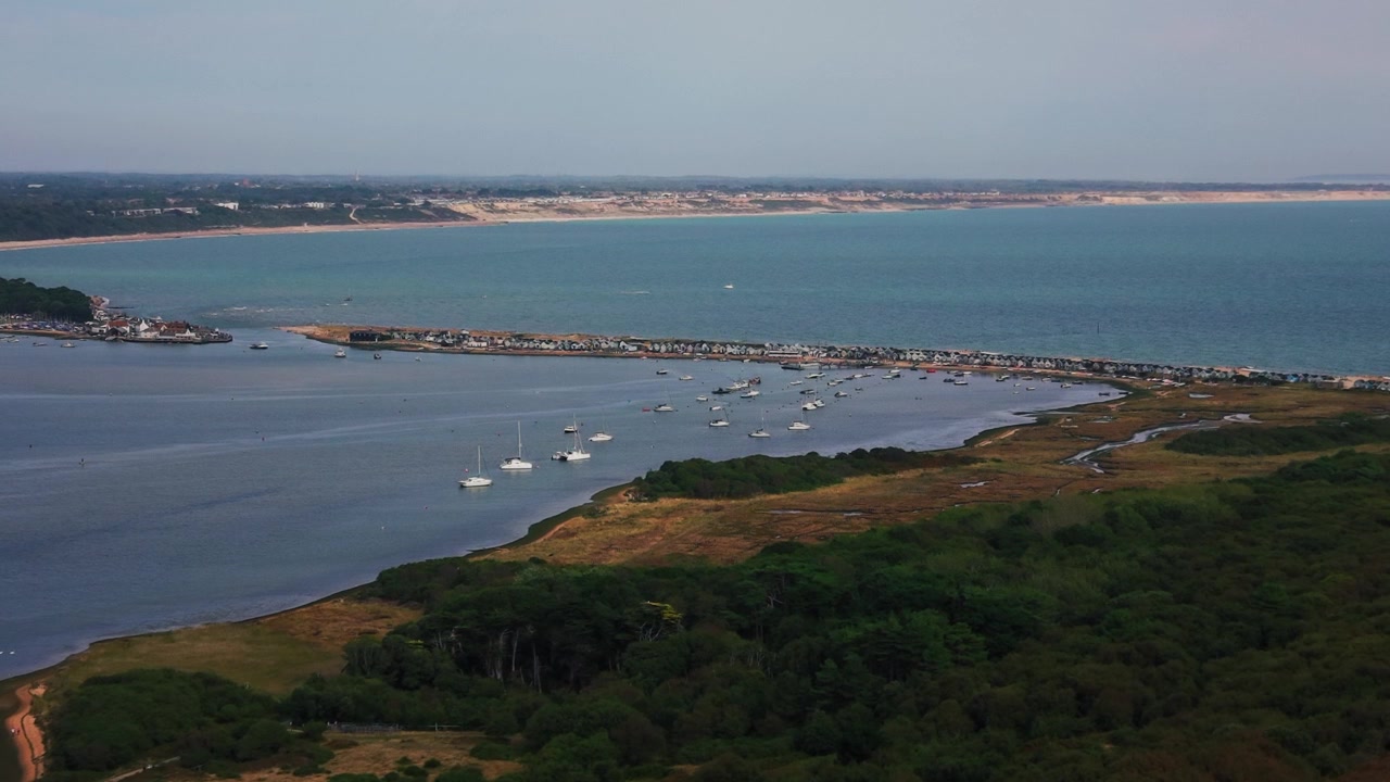 Ampia ripresa aerea che guarda attraverso il porto di Christchurch verso Hengistbury Head nel Dorset, Inghilterra. Barche ormeggiate, zone umide costiere e la stretta linea di costa si trovano tra il porto riparato e l'oceano