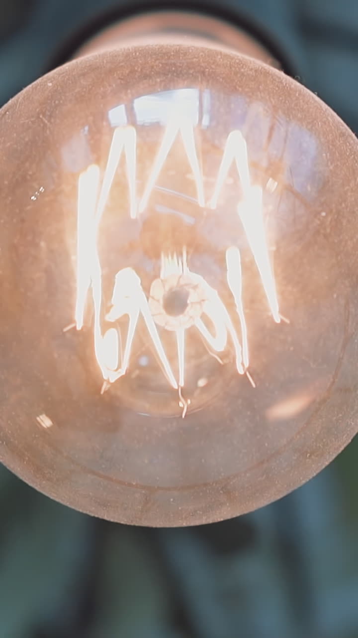 Bright glowing light-bulb in metal carcass hangs on ceiling in room extreme close low angle shot. Contemporary hall interior decor. Electricity and light