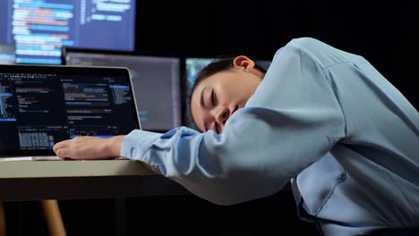 vista de atrás de una programadora asiática durmiendo mientras escribe código por una computadora portátil usando múltiples monitores que muestran la base de datos en los escritorios de ventana de terminal en la oficina