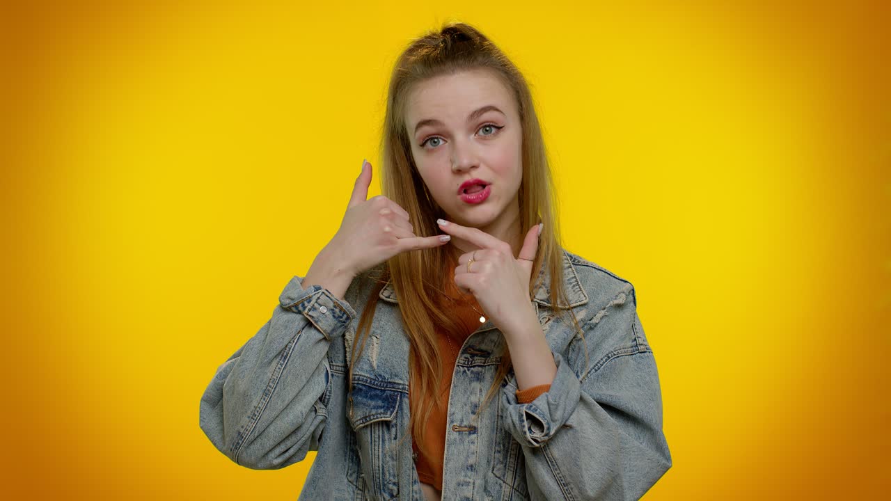 젠임 재을 입은 쾌활한 소녀가 카메라를 바라보며 전화 제스처를 하고 있습니다.