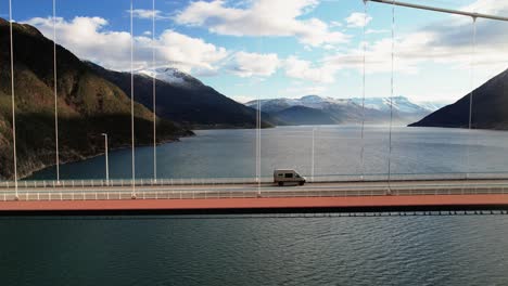 van crossing a scenic mountain bridge over a calm fjord under a bright sky