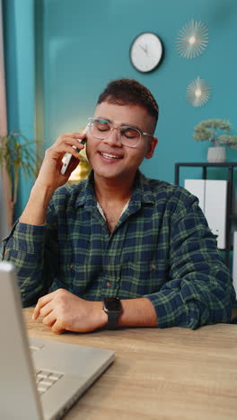 Un-Joven-Feliz-Y-Emocionado-Haciendo-Una-Conversación-Telefónica-Con-Un-Cliente-O-Colega-Sentado-En-Casa