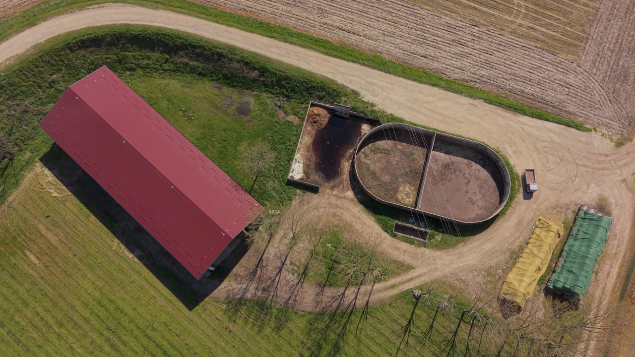 Aerial view of an open manure lagoon and barn on an Italian farm, showing storage and processing of liquid fertilizer before field application.