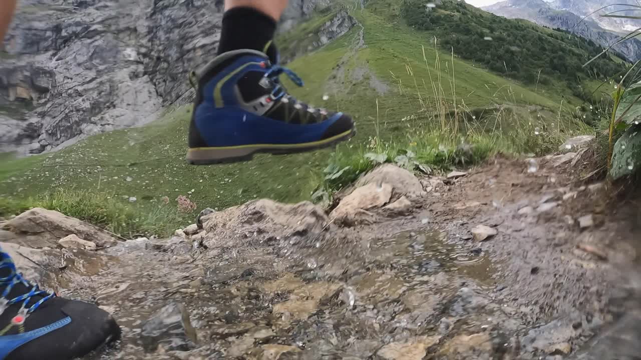 Un uomo cammina su un sentiero naturale nelle Alpi svizzere e schizza acqua con le scarpe da un piccolo ruscello che scende dalla montagna, Obvaldo, Engelberg, vista laterale.
