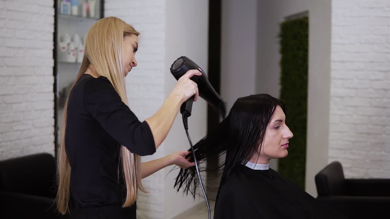 Caucasian brunette young woman get her hair dry by beautician barber after before the new haircut in hairdresser salon. Beauty industry. Side view