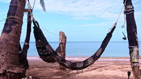 hamaca tejida colgada entre dos postes en una playa tropical junto al mar