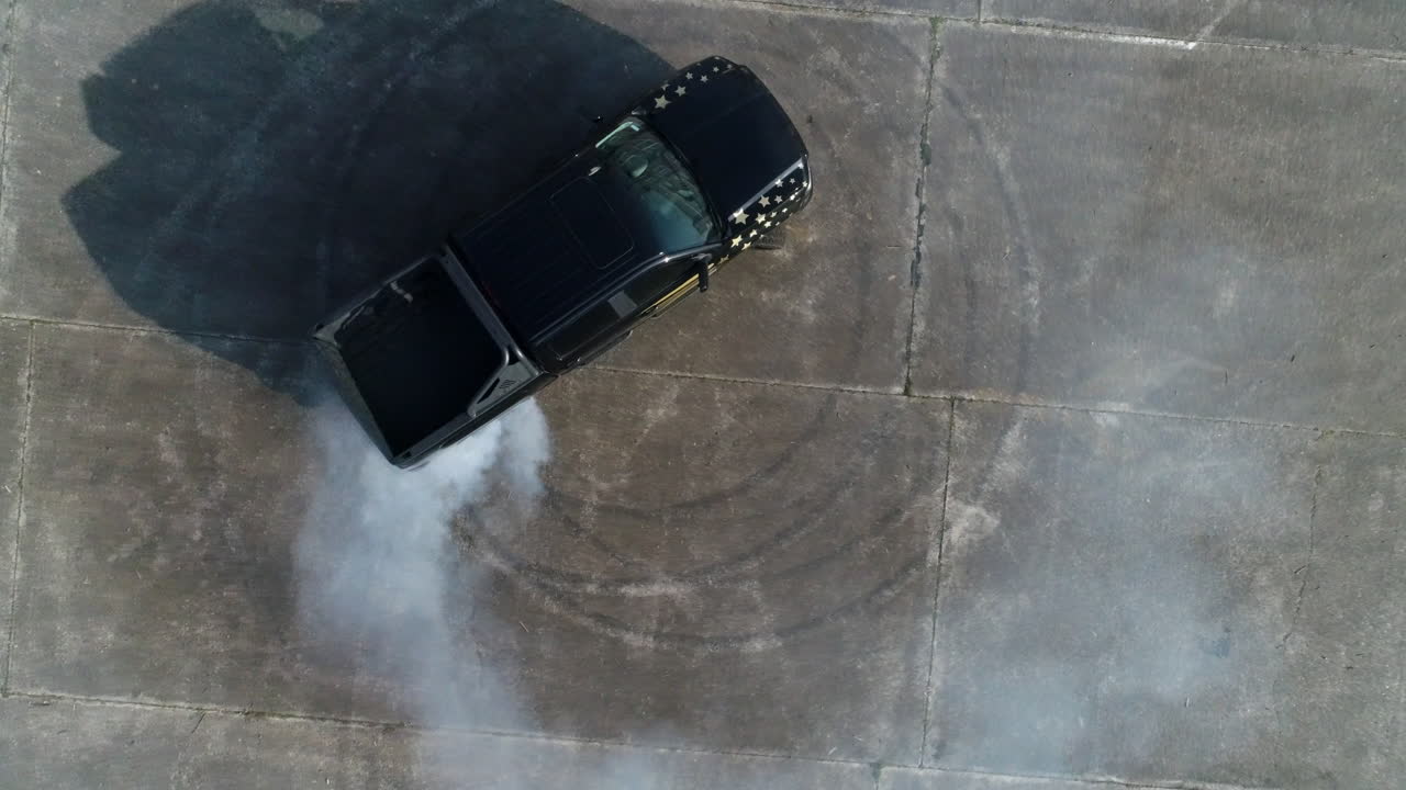 aerial: foto de un camión negro haciendo rosquillas en un estacionamiento abandonado