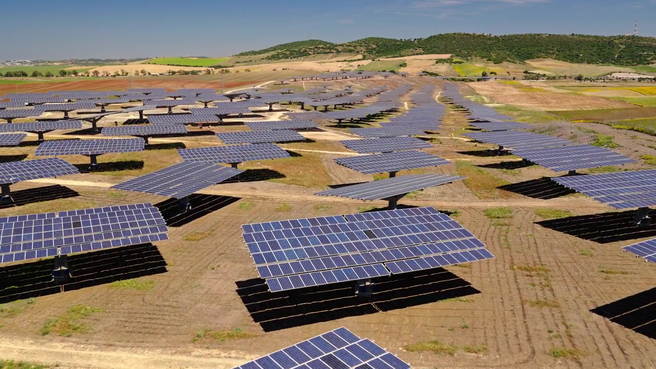 Filmato cinematografico con drone che sorvola un grande impianto fotovoltaico con pannelli che generano elettricità pulita e rinnovabile. Infrastruttura energetica sostenibile a supporto della transizione energetica globale.