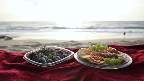 tabla de embutidos, tabla de quesos en alfombra roja durante un picnic en la playa al atardecer