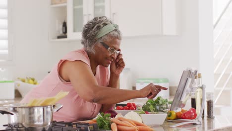 Happy-senior-african-american-woman-cooking-in-kitchen,-using-tablet