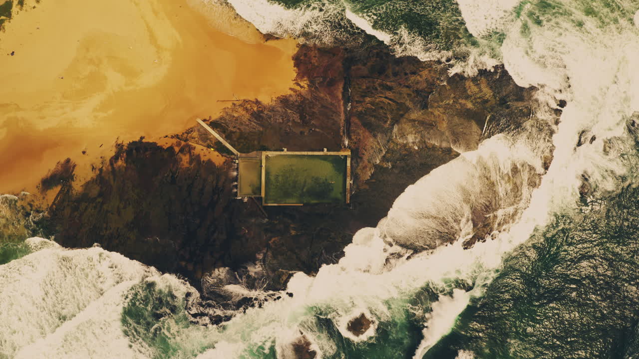 Waves crashing around and spilling into a tidal pool at Mona Vale Beach on the northern beaches area of Sydney