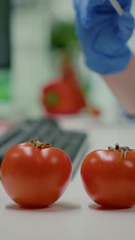 close-up of a scientist's gloved hand injecting a syringe into a tomato, representing genetic modification or food research
