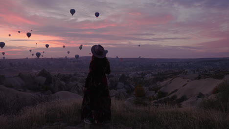 girl running towards a cliffside to get a better view of hot air balloons in flight in cappadocia turkey - panning shot