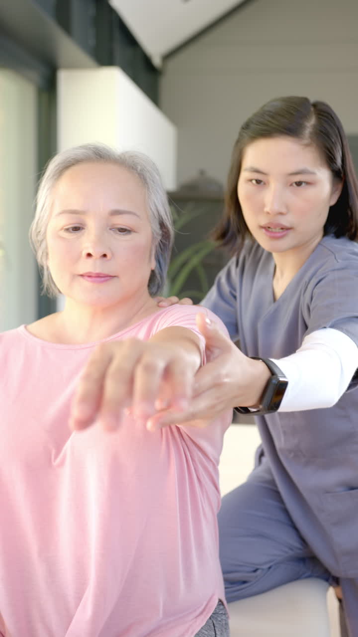 Vertical video: Assisting senior woman with arm exercises, physiotherapist conducting home therapy s