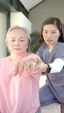 vertical video: assisting senior woman with arm exercises, physiotherapist conducting home therapy s