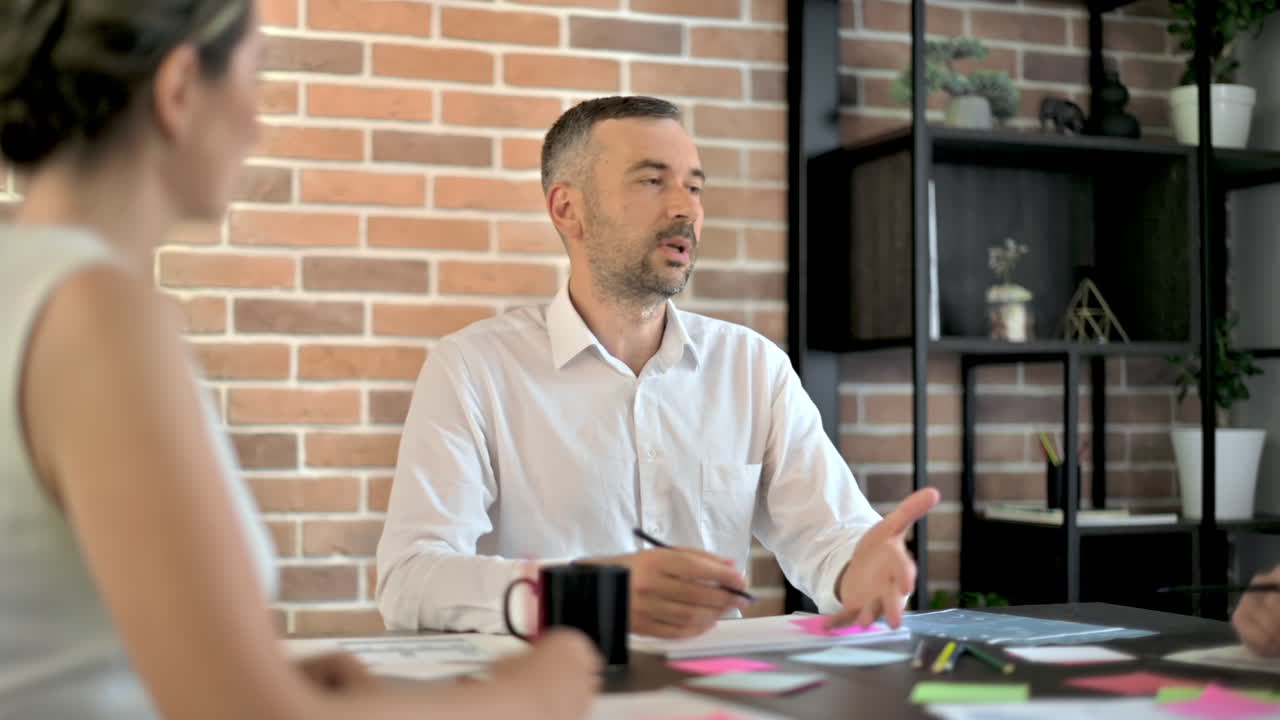 Tre persone stanno lavorando e parlando in ufficio. Documenti con grafici e informazioni