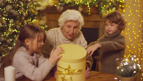 grandmother and grandchildren open gift at christmas, grandmother puts woolly hats on her grandchildren