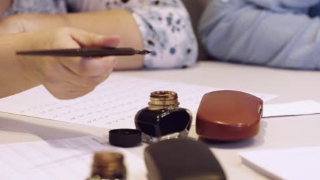 Mano-Femenina-Escribiendo-Pluma-De-Tinta-Negra-De-La-Vieja-Escuela-En-La-Hoja-Blanca-De-Papel-De-Cerca-En-Cámara-Lenta