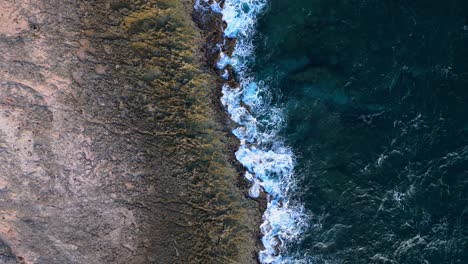 drone top down pan across jagged rocky shoreline with volcanic basalt and sharp edges in water