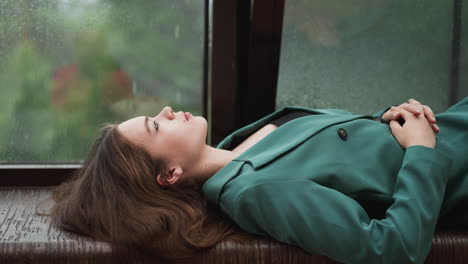 woman sitting by a window, looking out at the rain