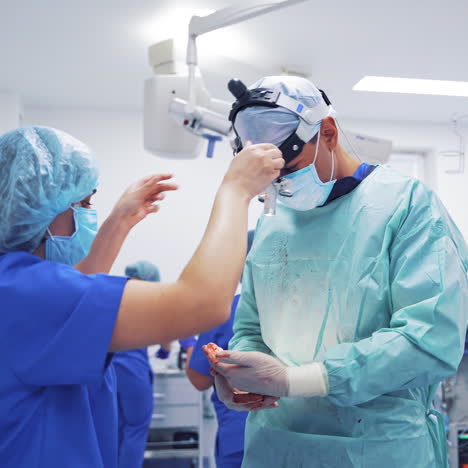 professional doctor and a woman in medical uniform in the operating room. female assistant helps to correct the magnifying glasses on surgeon's head.