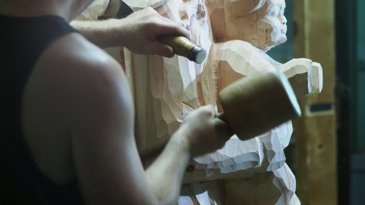 Wood sculptor strikes with a mallet and guides a chisel to refine a statue, showing the strength, precision, and artistry of traditional wood carving in progress