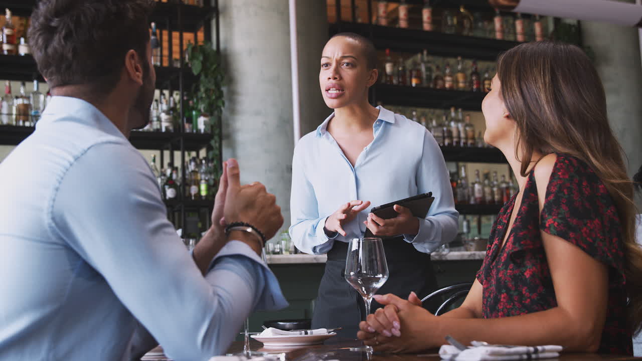 Female Waitress With Digital Tablet Taking Order From Romantic Couple Sitting At Restaurant Table