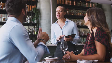 female waitress with digital tablet taking order from romantic couple sitting at restaurant table