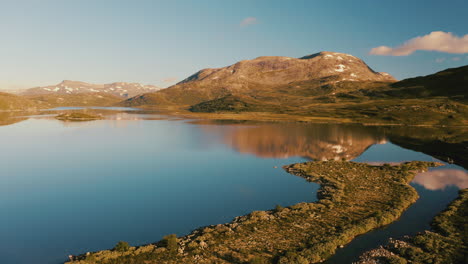 mountain and sky reflections over the calm water of vavatnet lake during golden hour sunrise in hydalen, hemsedal, norway