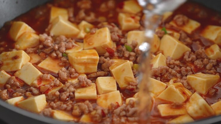 Cooking mapo tofu. Stir-frying tofu with hot spicy sauce in a pot at home.