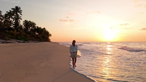 an aerial drone captures a peaceful moment as a woman walks along the untouched shoreline of geiymiskih fannu beach in fuvahmulah, maldives.