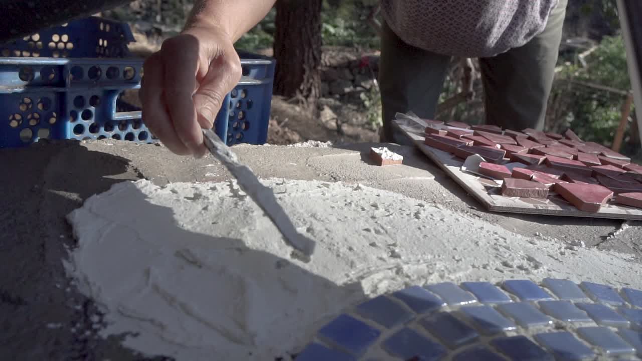 Slow motion of woman's hands spreading glue on mosaic tiles