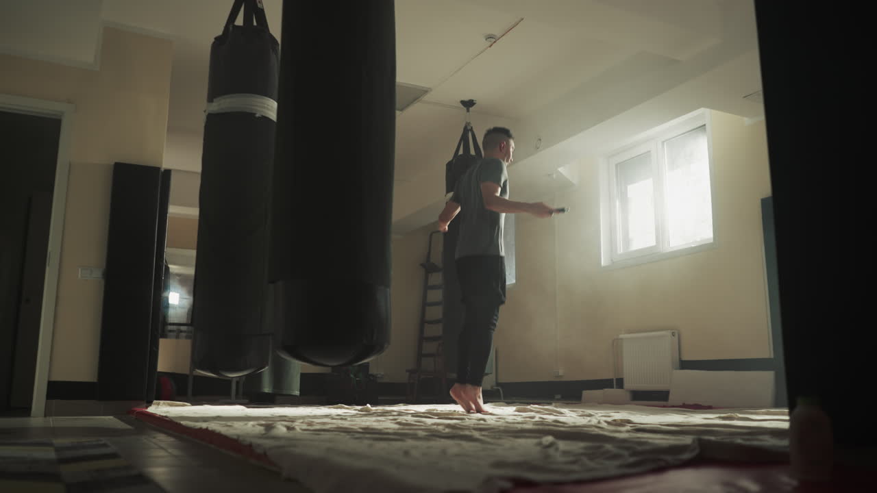 hombre deportivo hace ejercicios con cuerda de salto en el gimnasio. kickboxer muscular salta en cuerda de saltado en el club de artes marciales en cámara lenta. desarrollo de resistencia corporal