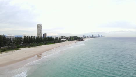 blue water of burleigh beach with a view of beachfront apartment buildings and rocky cliff in gold coast city, australia