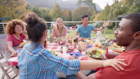 happy diverse group of friends eating and talking at dinner table in garden, slow motion