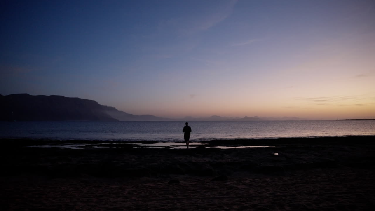 hombre caminando por la playa mientras toma fotos del mar durante el anochecer en lanzarote, españa