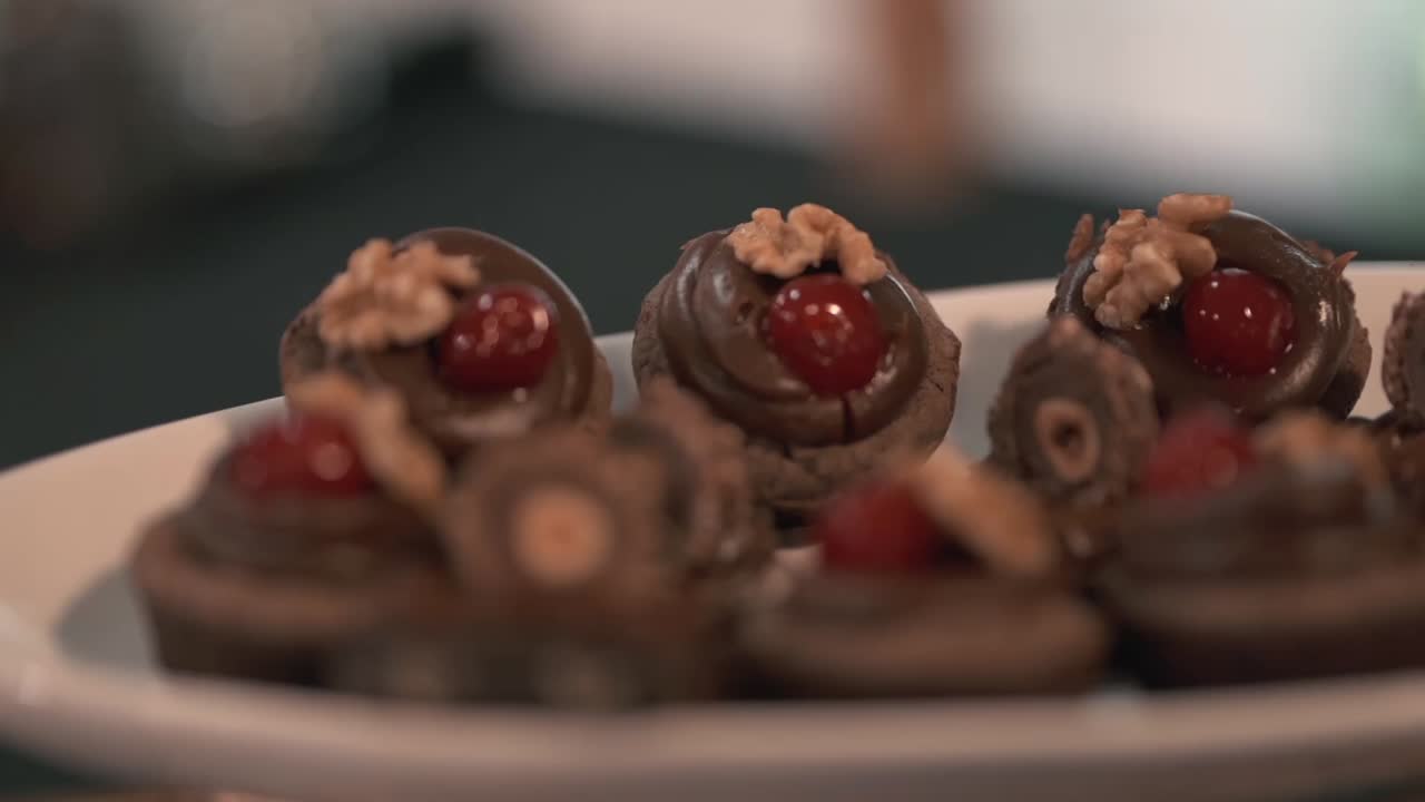 Carrellata a destra su un piatto di dolci, con messa a fuoco su cioccolatini gourmet guarniti con ciliegie e noci a un tavolo di catering di lusso per matrimoni