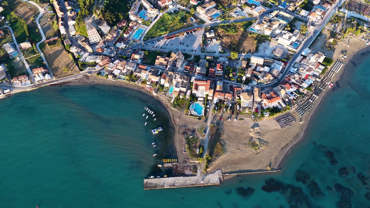 Vista aérea superior da vila de Sidari e praia de areia no Norte de Corfu, Grécia, com mar turquesa, barcos, resorts e costa mediterrânea.