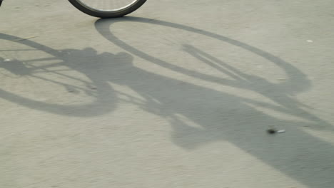 cyclist wearing sneakers and black trousers pedaling bicycle slowly on a sunny day, creating distinct and clear shadow of the bicycle cast onto the sunlit road