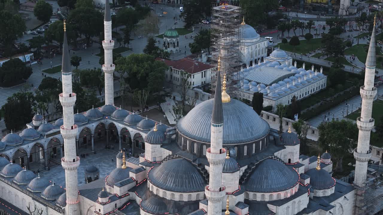 Moschea blu con cupole grigie a cascata e alti minareti slanciati che si affaccia su una vivace piazza urbana