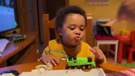 impatient two-year-old black baby eats pizza at home fed by mum wth a fork
