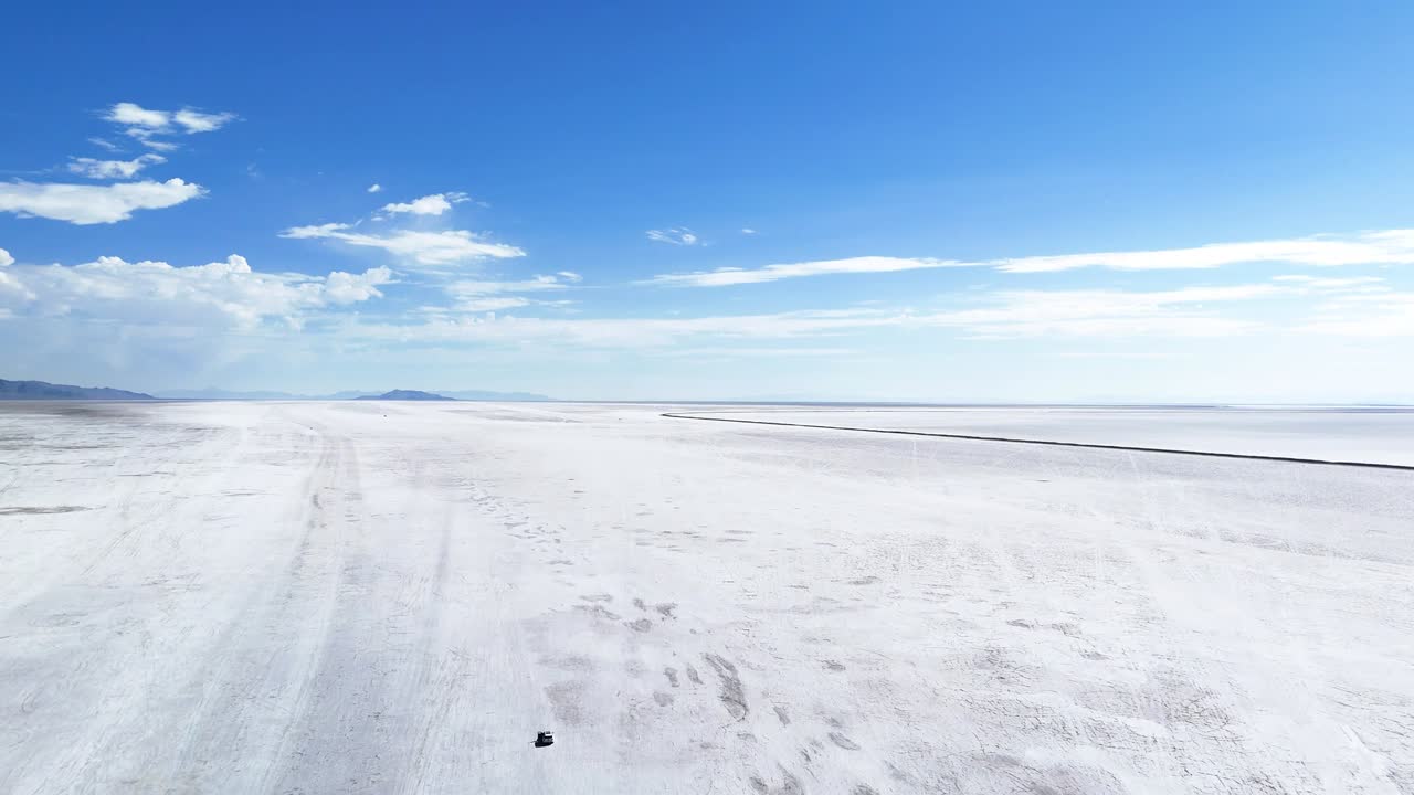 Aerial drone tilt up shot showing wide white salt flat stretching to horizon with vivid blue sky and distant mountains in remote West Virginia, highlighting contrast of terrain and open landscape