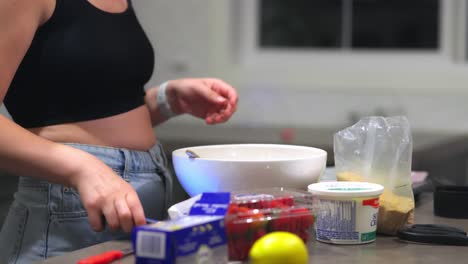 A-caucasian-woman-is-stirring-baking-ingredients-with-a-fork-and-then-picks-up-her-phone-to-check-the-cheesecake-recipe