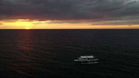 un solo bote conduce lentamente sobre las pacíficas olas del océano en la espectacular puesta de sol con nubes oscuras y pesadas que llegan a la isla cresta de gallo en filipinas